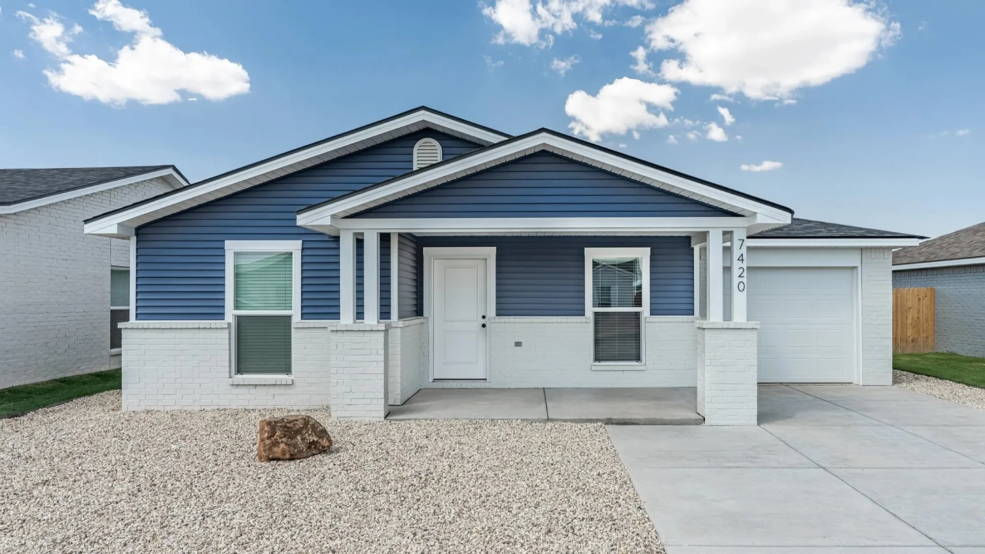 Front view of a modern house with blue siding, white brick accents, a white front door, and a attached garage, under a partly cloudy sky.