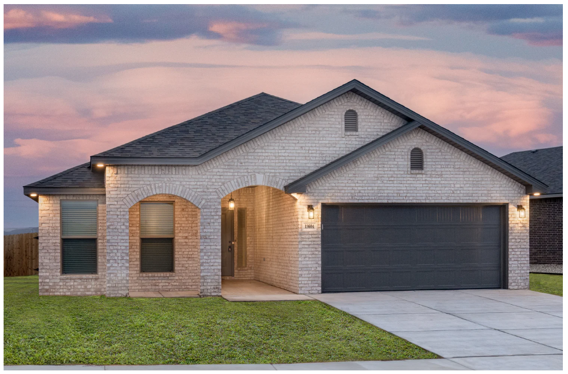 A modern single-story house with a brick exterior, a three-car garage, and a small front yard, photographed at dusk with a colorful sky.