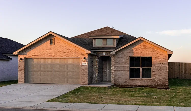 Front view of a brick house with a two-car garage, a small front porch, and a window on the right side, during daytime with a partly cloudy sky.