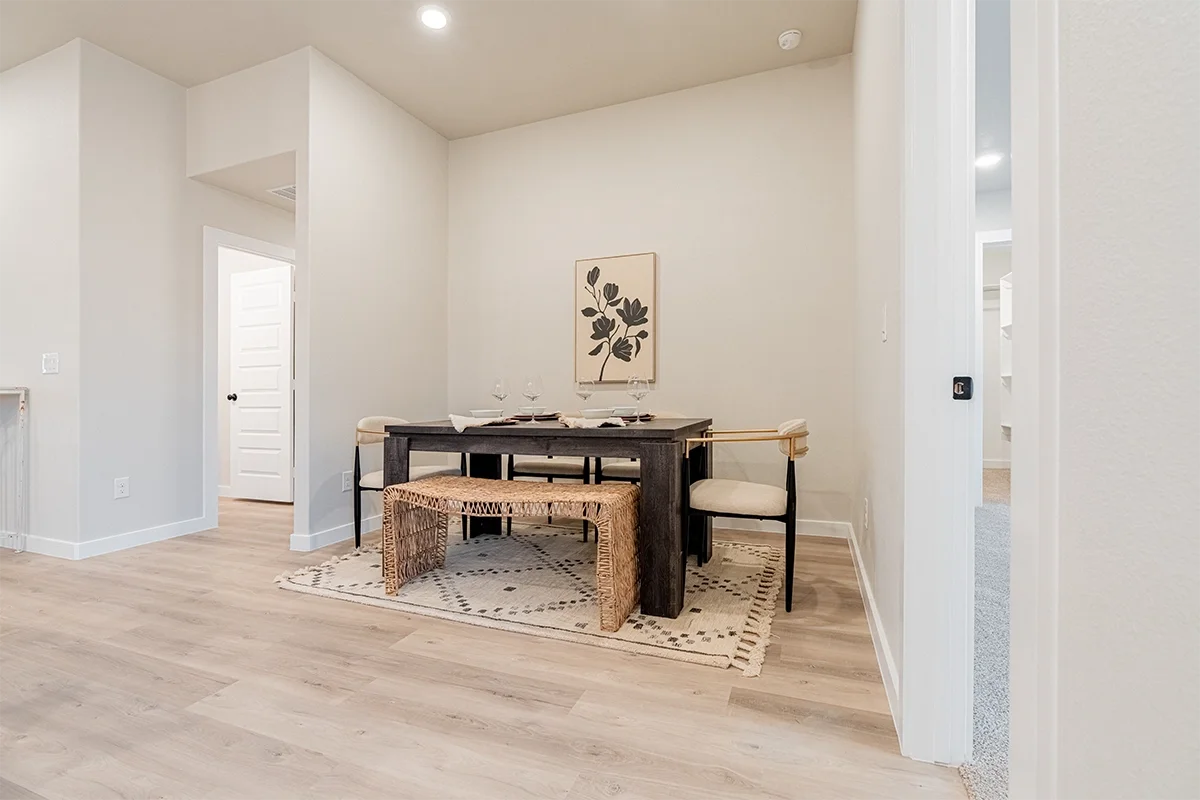 Empty dining room with a dark wood table, four chairs, and a beige rug, with a wall art featuring black leaves.