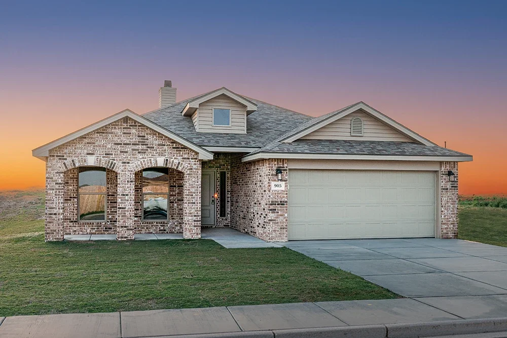 Brick house with a front porch, double garage, and a sunset sky in the background.