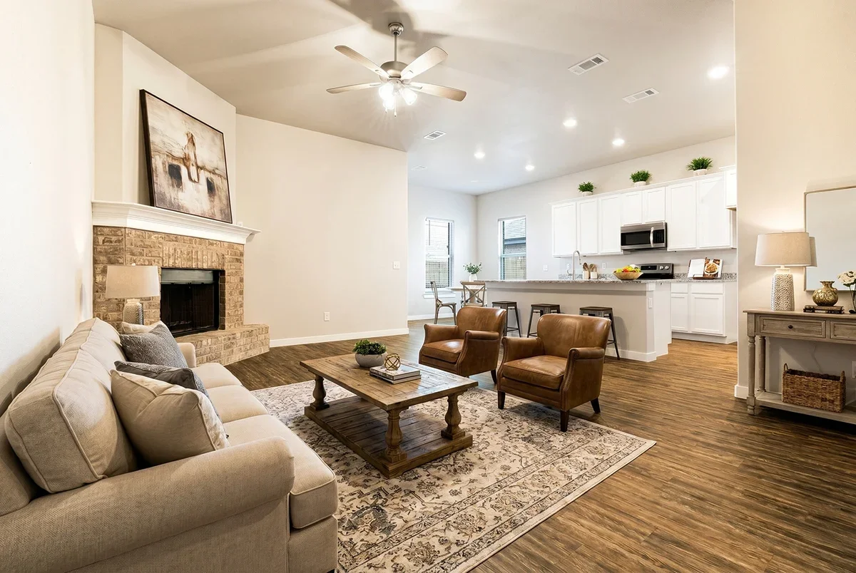 Living room with beige sofa, two brown leather armchairs, wooden coffee table, fireplace, and open kitchen with white cabinets and bar stools.