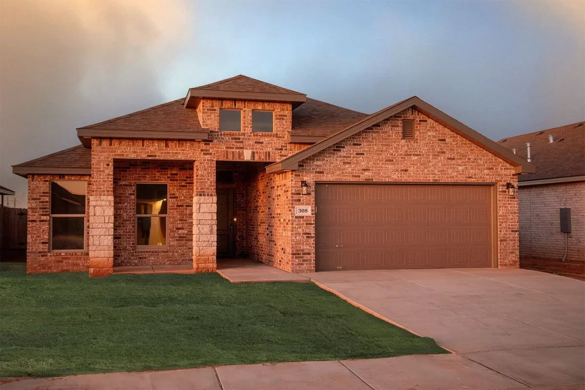 A two-story brick house with a front garage, front porch, and green lawn during sunset.
