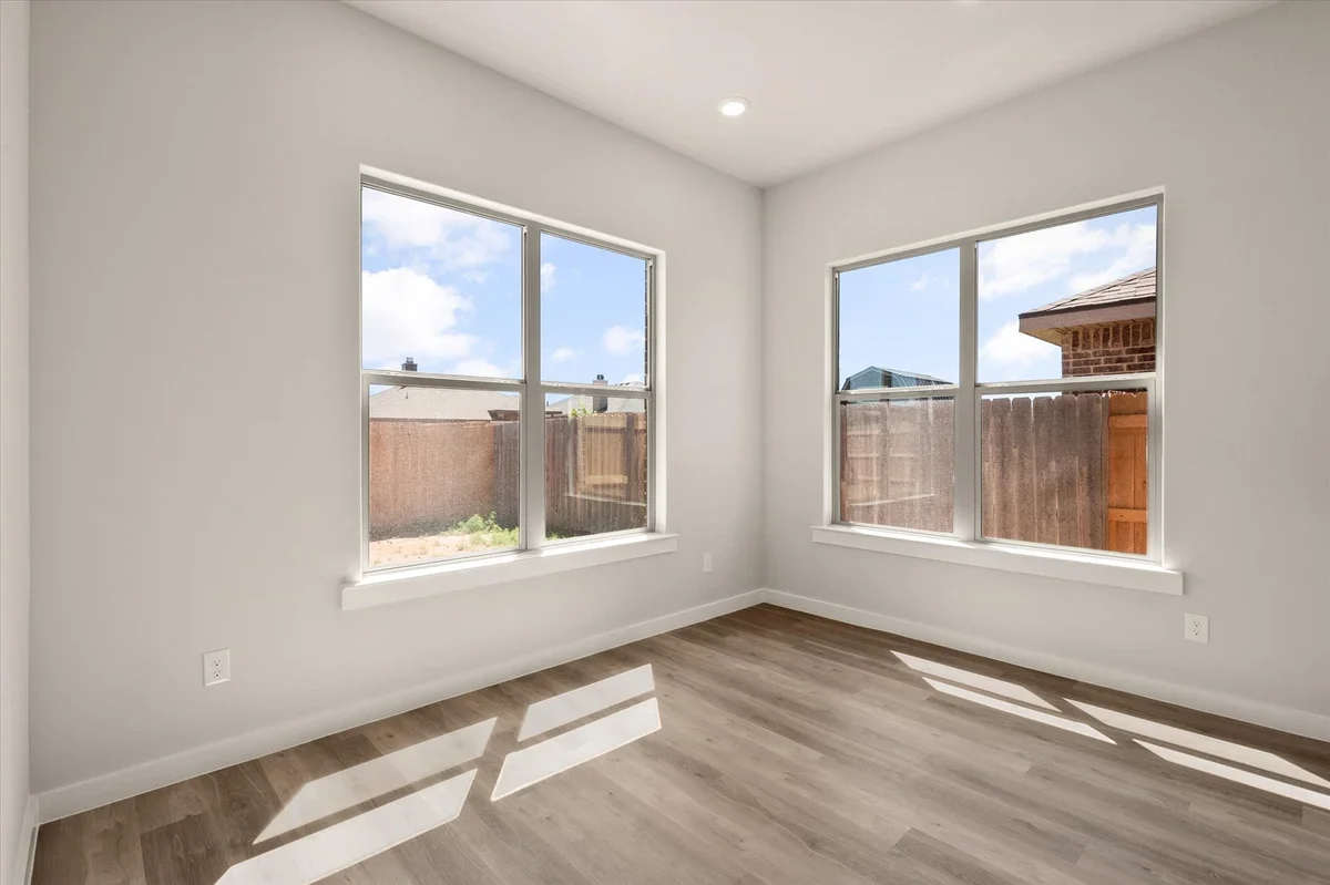 Empty room with white walls, large windows, and light wood floor, sunlight casting shadows.