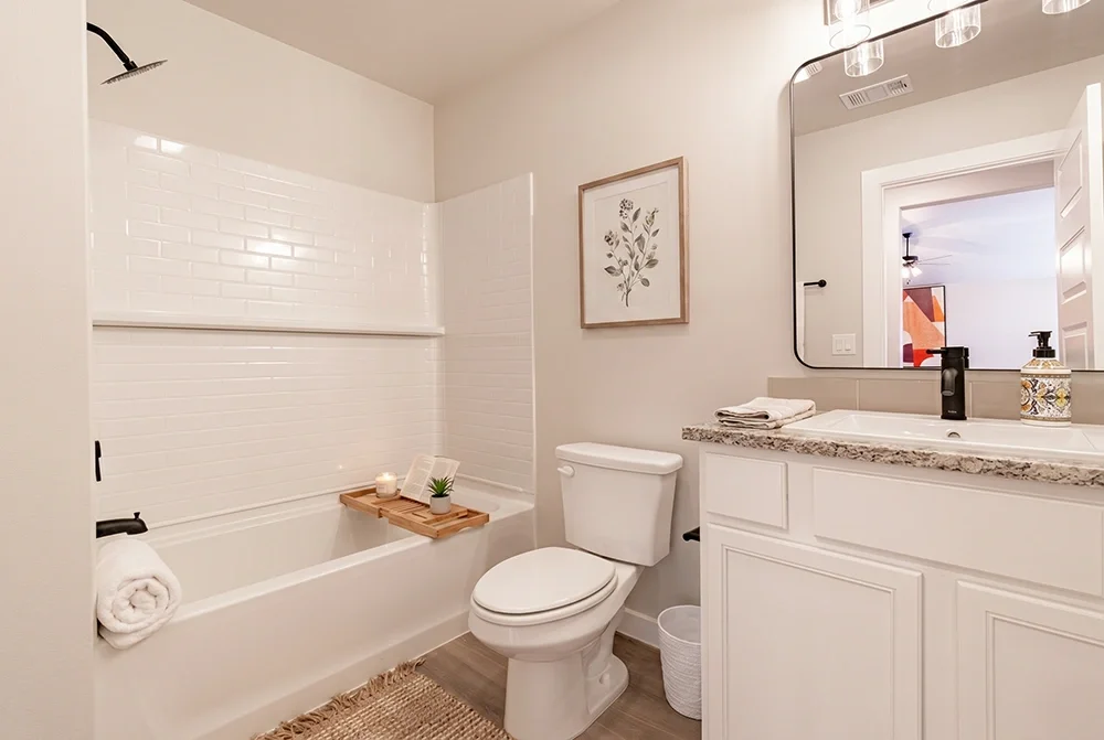 Bathroom with bathtub, toilet, white vanity with granite countertop, large mirror, framed botanical art, and decorative accents.