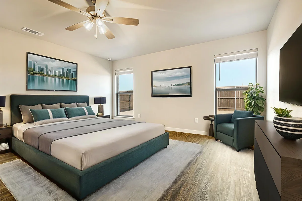 Modern bedroom with a large bed, pillows, wall-mounted TV, ceiling fan, and windows with views of a balcony and water scene.