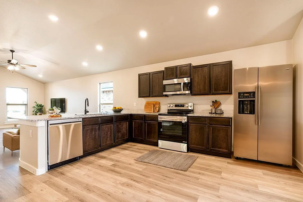 Modern kitchen with dark wood cabinets, stainless steel appliances, granite countertops, a kitchen island, and light wood flooring.