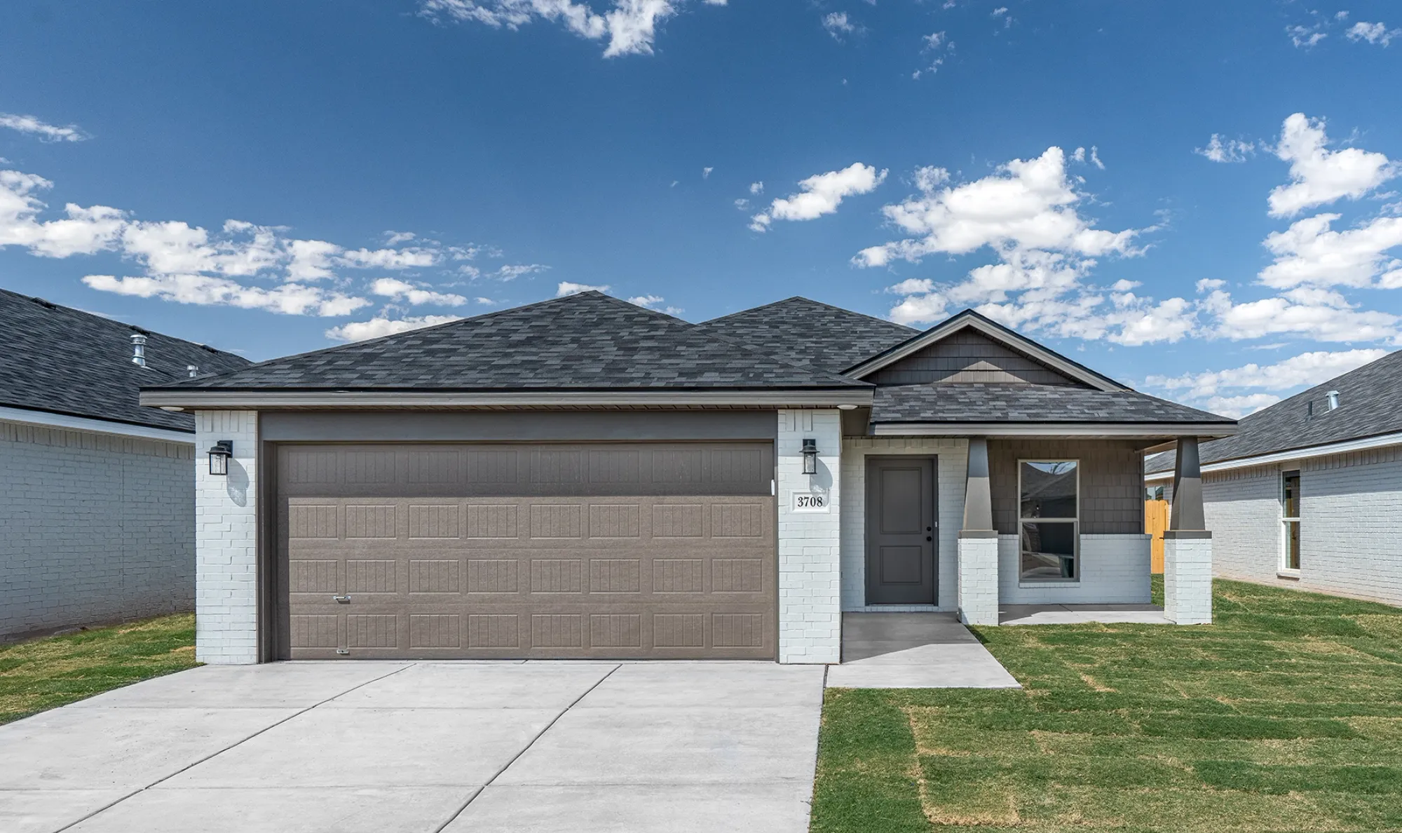 Front view of a modern suburban house with a gray garage door, white brick exterior, gray front door, small covered porch, and a well-maintained lawn under a blue sky with scattered clouds.