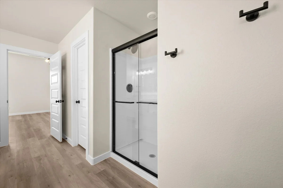 Bathroom interior with a glass shower enclosure, open closet doors, and hooks on the wall.