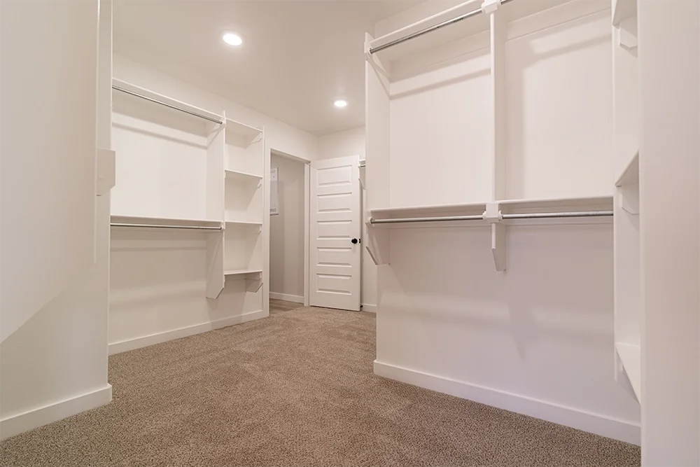 Empty walk-in closet with white walls, built-in shelves, and hanging rods, carpeted floor, and a closed white door.