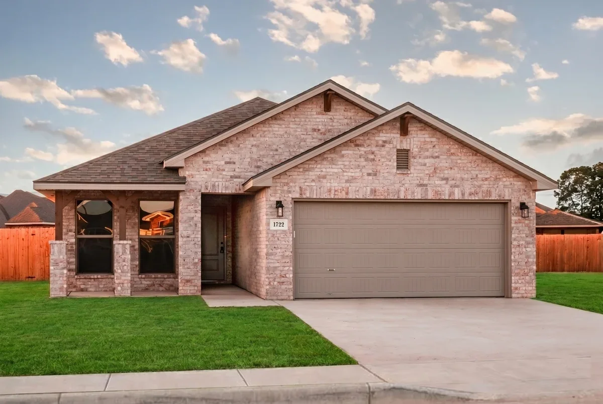 Front view of a brick house with a two-car garage, a small porch, and a green lawn under a partly cloudy sky.