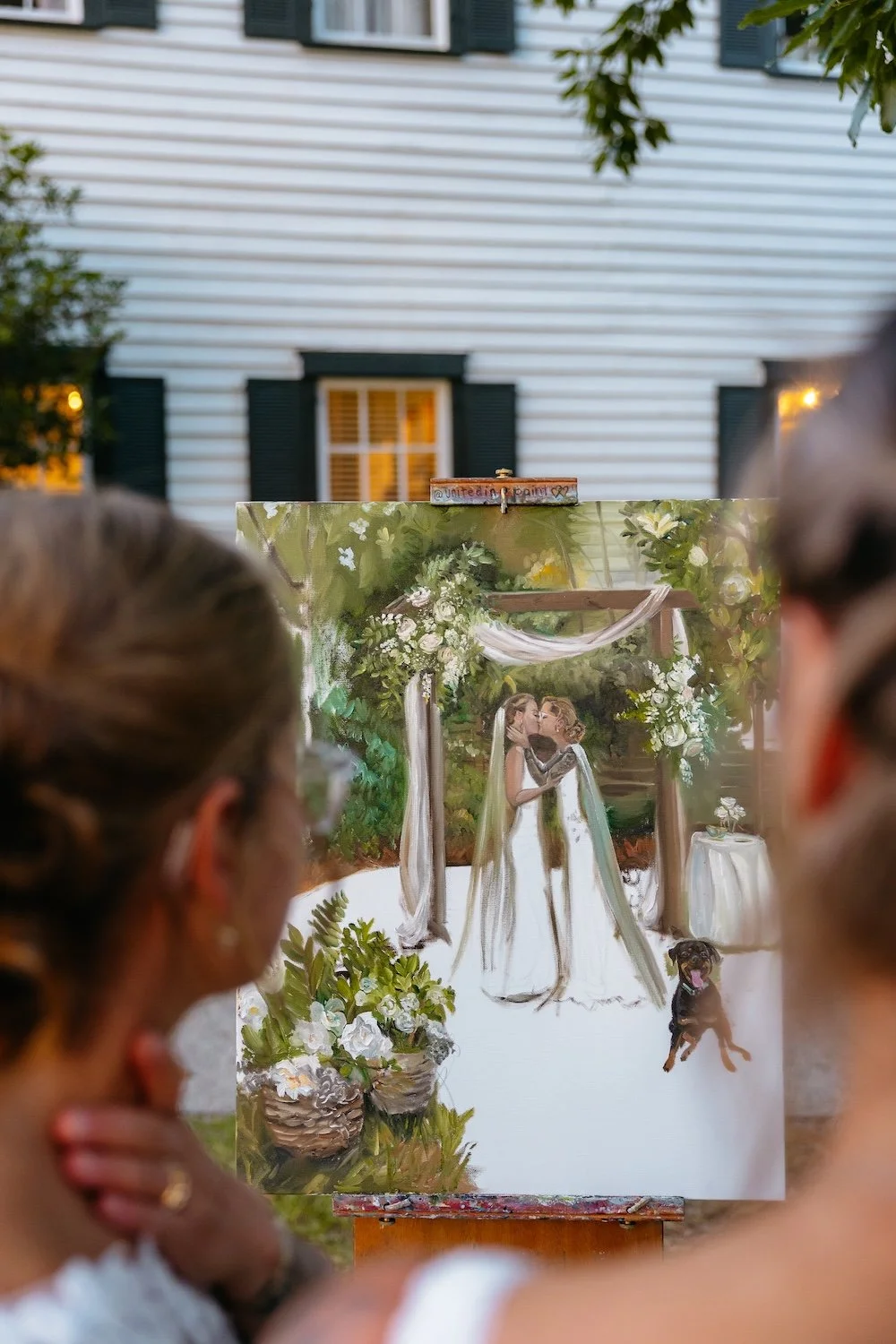 two brides look at their live wedding painting that is partially finished