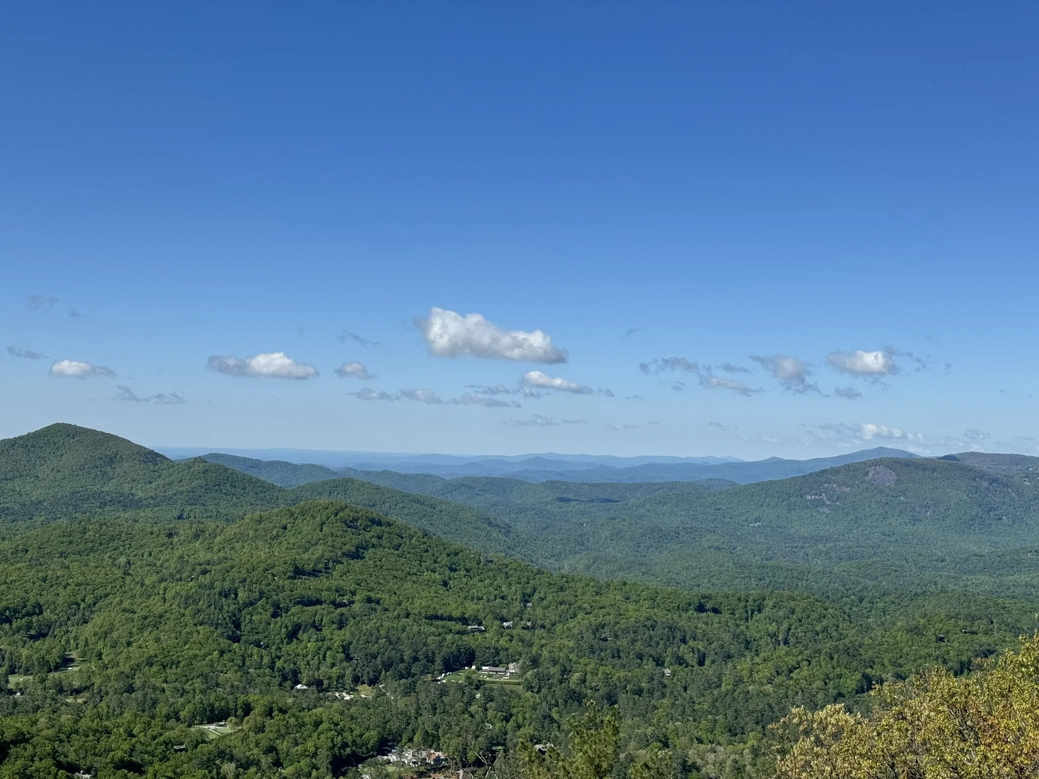 A scenic view of green forested mountains under a blue sky with scattered clouds.