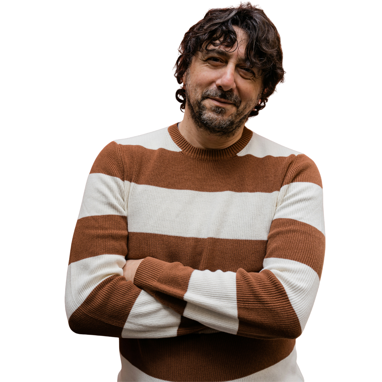 A man with curly brown hair and a beard, wearing a brown and white striped sweater, stands with his arms crossed and a slight smile.