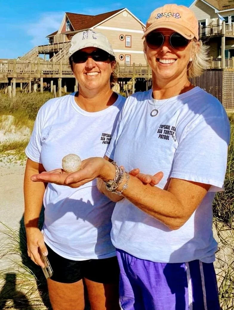 Turtle patrol volunteers smiling with a baby sea turtle egg after a hatching