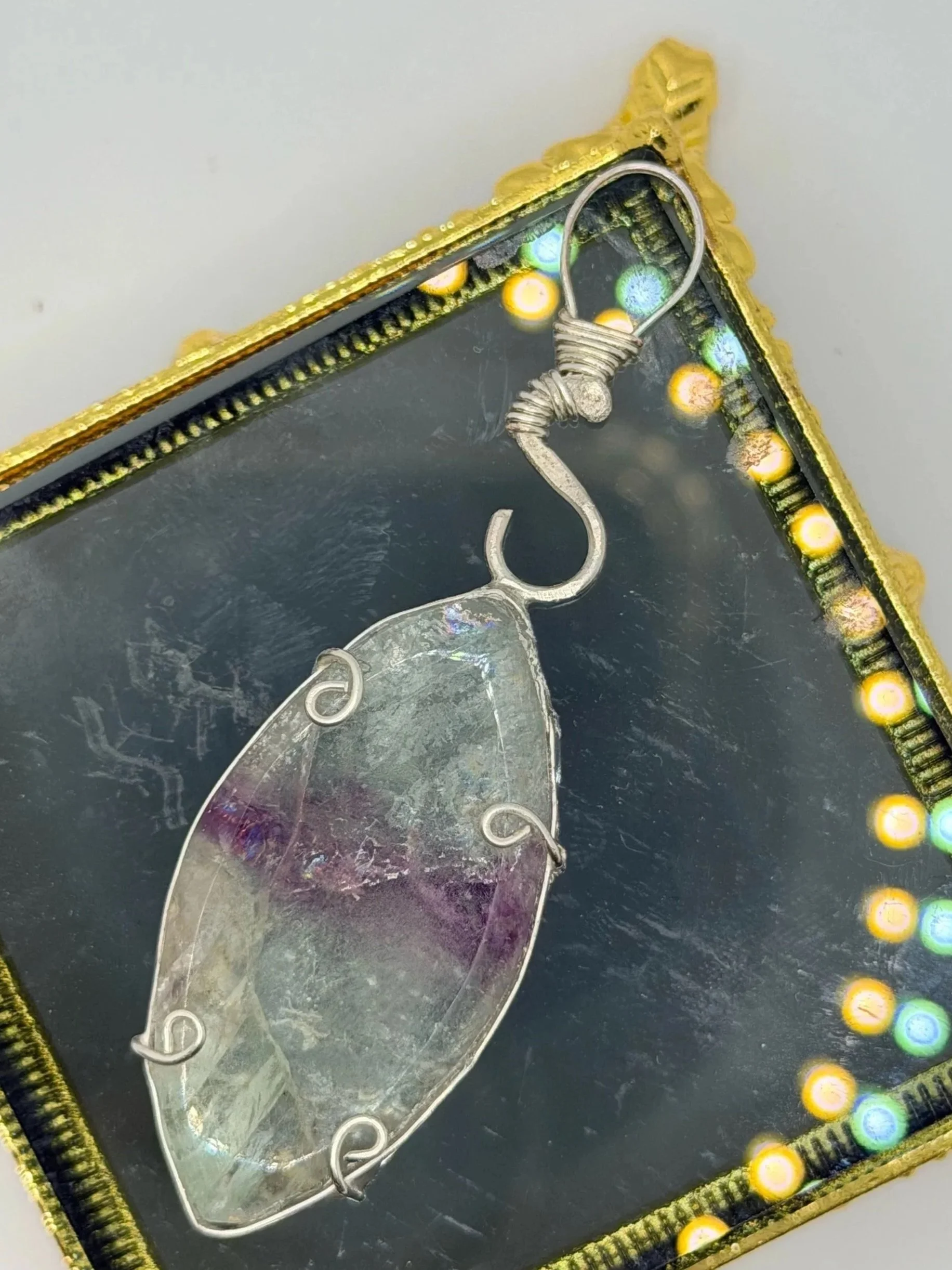 A jewelry pendant featuring a blue and green triangular stone wrapped with copper wire, hanging on a plain white background.