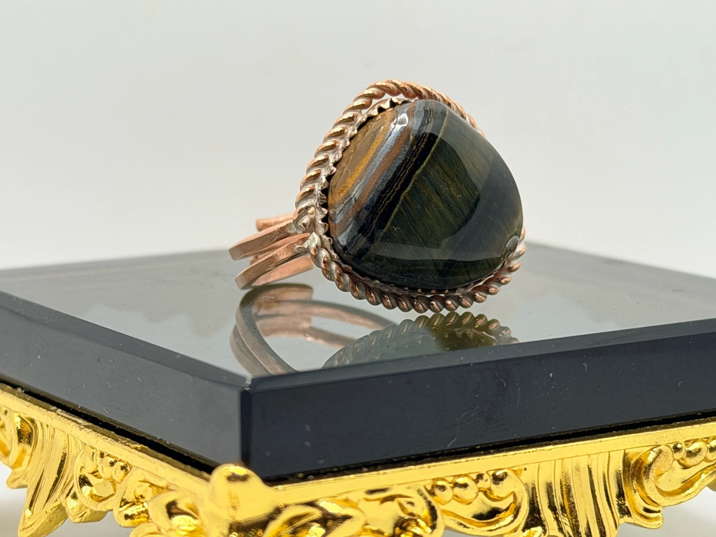 A ring with a large black and iridescent gemstone on a metal pole with a copper-colored wire wrapped around the pole.