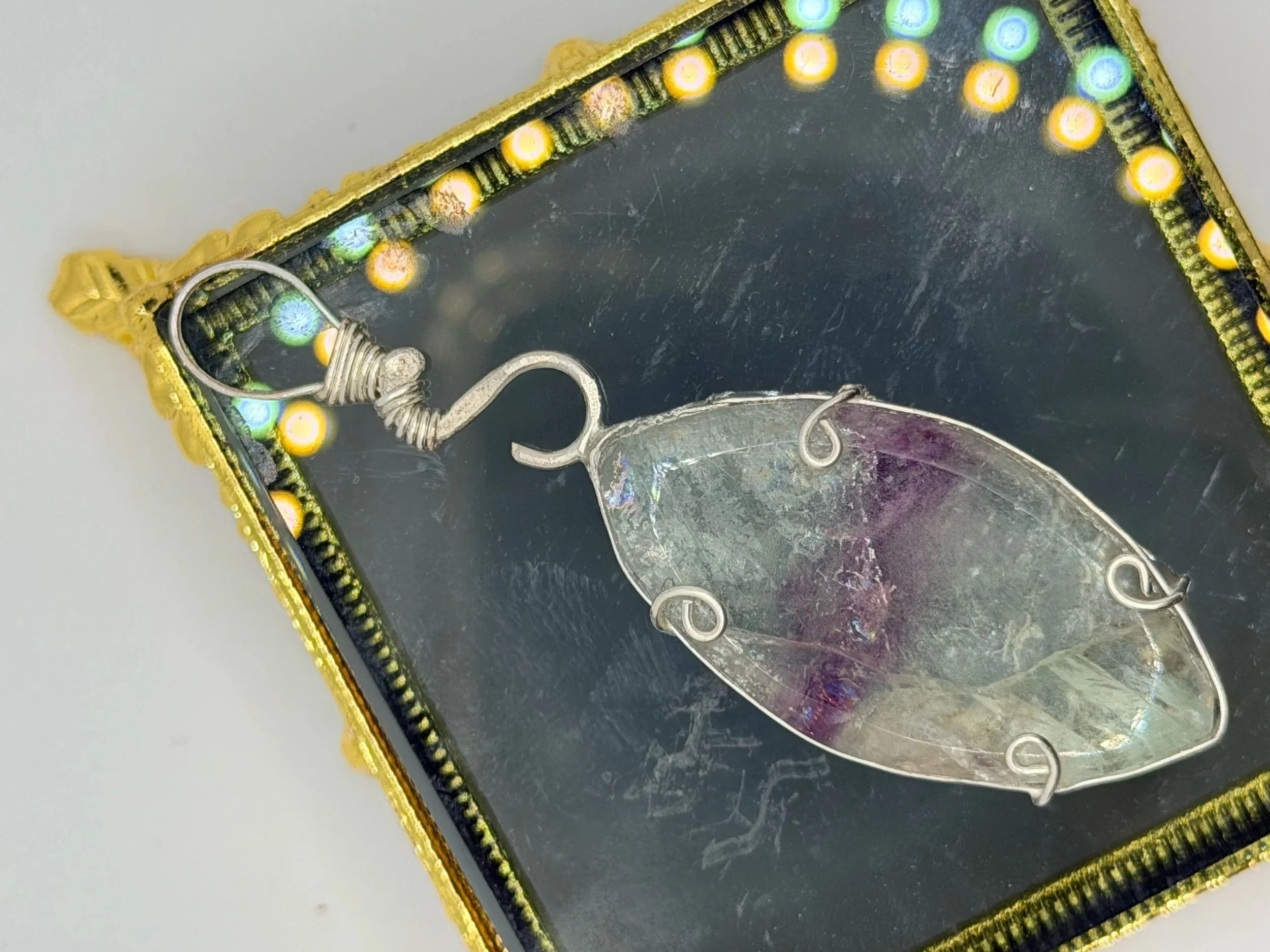 A jewelry pendant featuring a blue and green triangular stone wrapped with copper wire, hanging on a plain white background.
