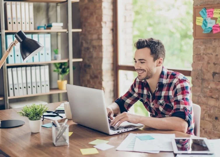 cheerful-young-brunet-freelancer-is-smiling-typing-on-his-laptop-in-picture-id932763106.jpg