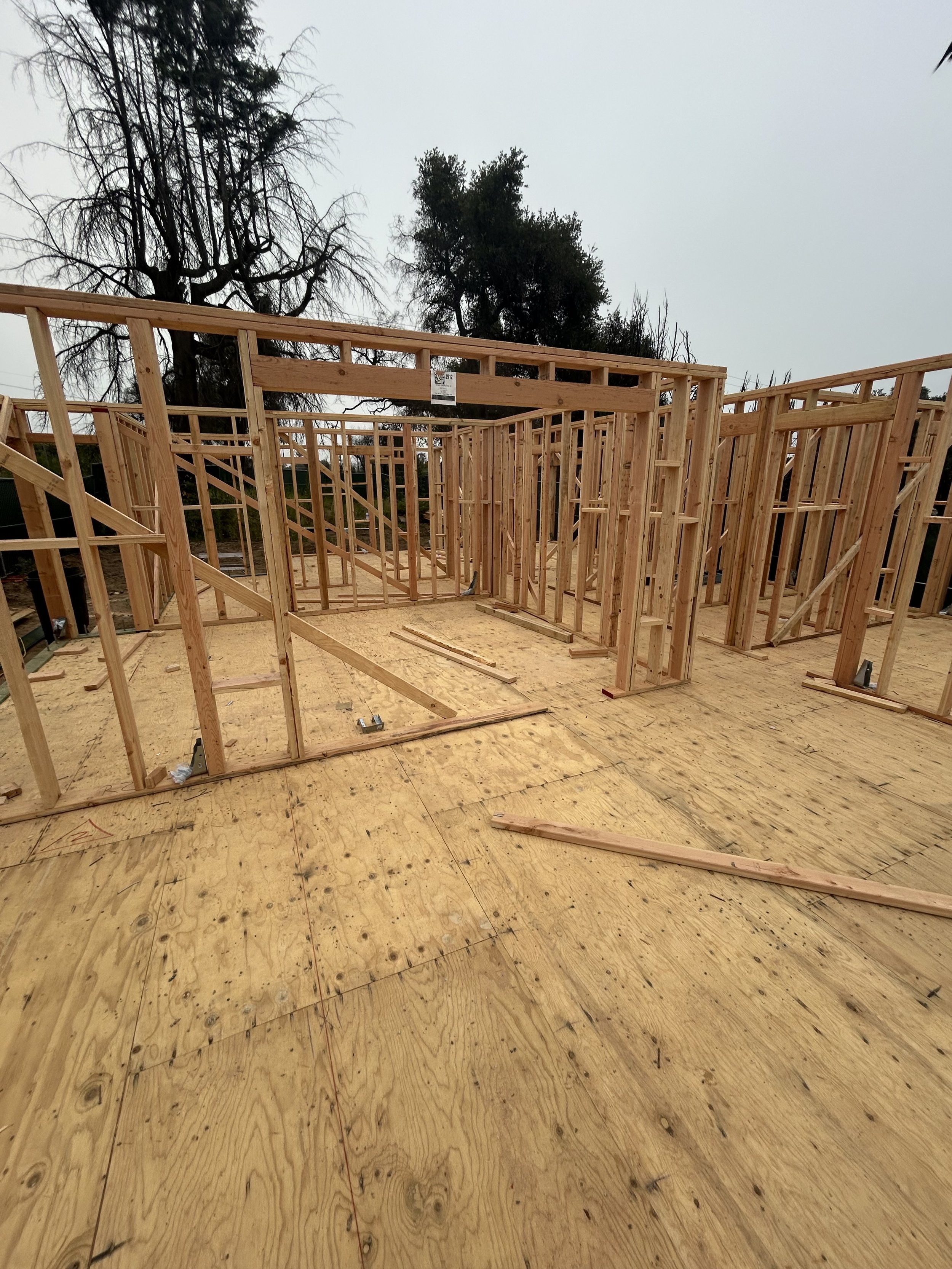 Wooden framing of a house under construction with plywood floors and an overcast sky.