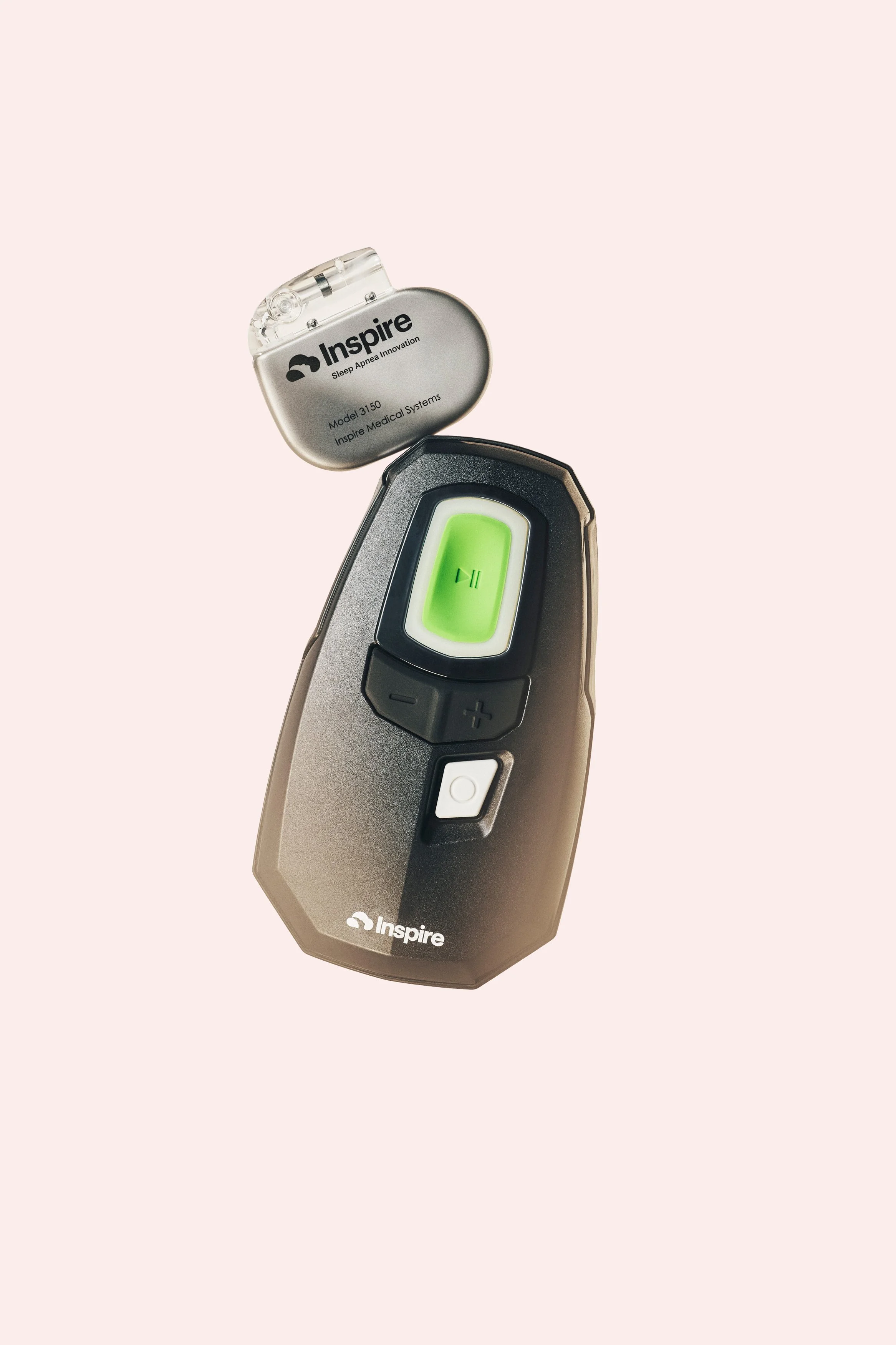A black Inspire portable device with a green pause button and white power button, along with black volume control buttons, placed on a light pink background.