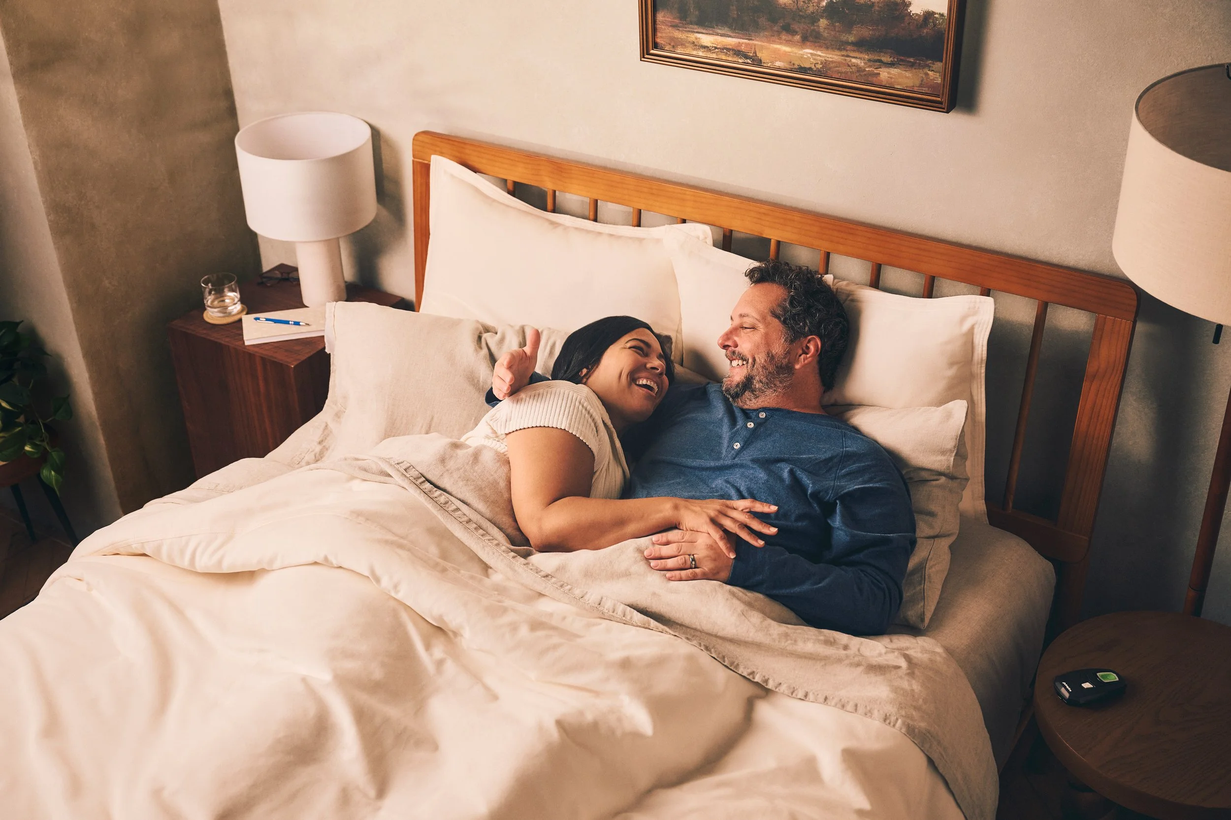 A couple lying in bed, smiling and looking at each other