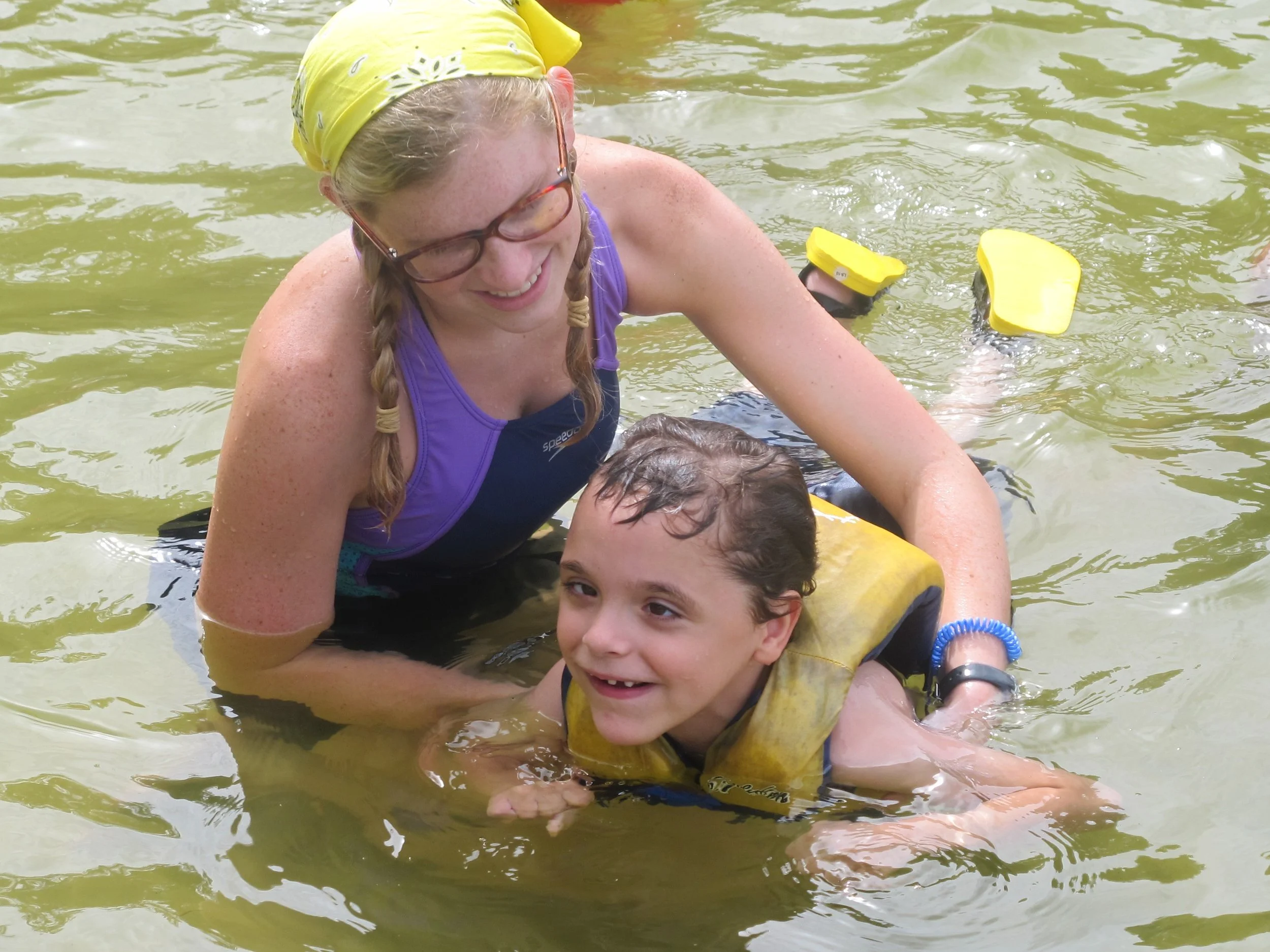 a boy with a disability swimming in the lake with the help of his female counselor