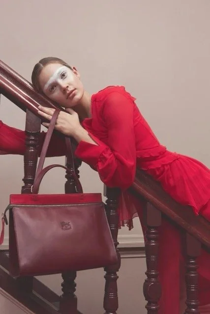 Young woman in a red dress leaning on a staircase railing next to a red handbag