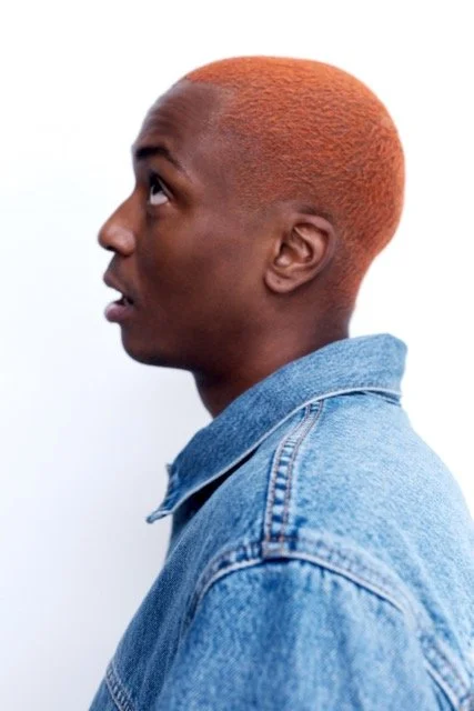 Side profile of a person with reddish-orange hair wearing a blue denim jacket.