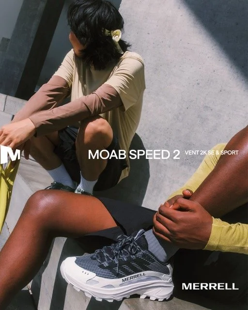 Two people sitting outdoors on concrete steps, one with crossed arms and the other with hands clasped, wearing athletic clothing and sneakers, with sunlight casting shadows.