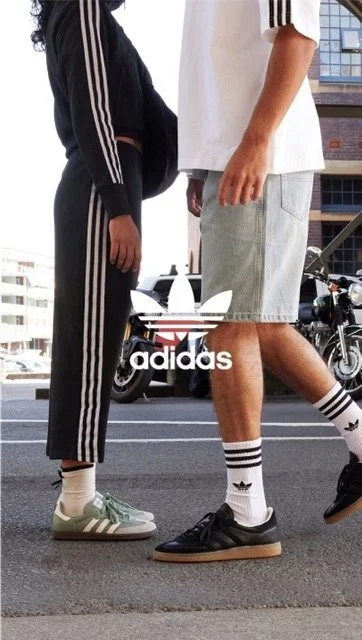 Close-up of two people standing face-to-face on a city street, wearing Adidas sportswear and sneakers with the Adidas logo visible.