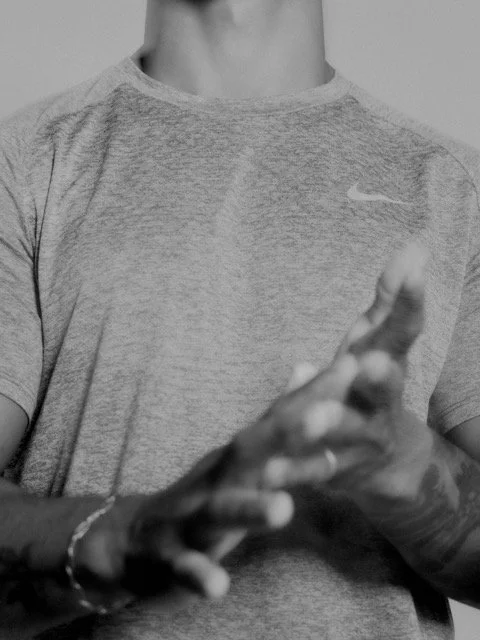 Close-up of a person wearing a Nike t-shirt with tattooed hands clasped together.