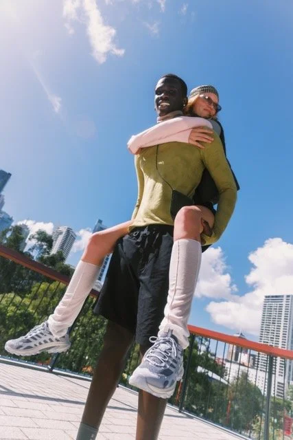 A man giving a girl a piggyback ride outdoors on a sunny day with blue sky and buildings in the background.