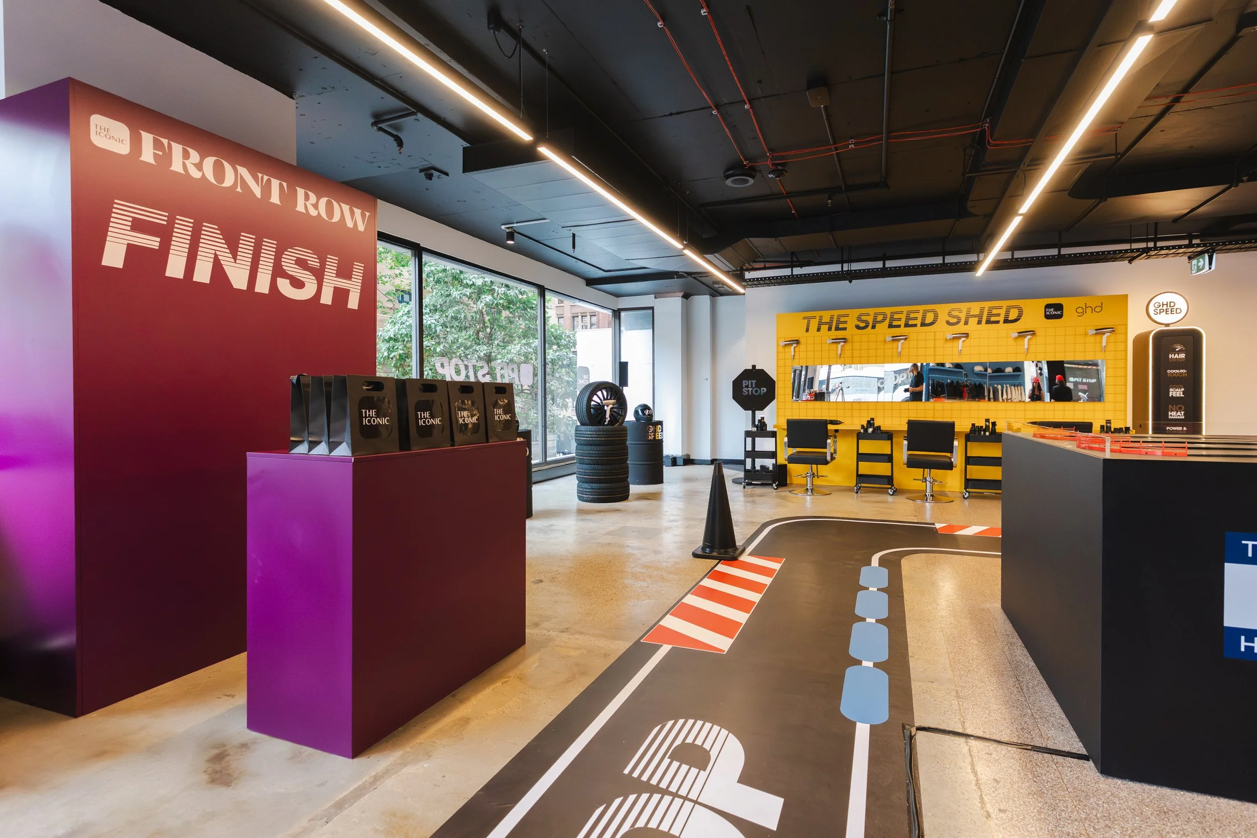Interior of an activity center with a large red sign that says 'Finish' and a yellow sign that says 'The Speed Shed.' There are tires, chairs, and a pit stop sign, indicating a racing or driving simulation area.