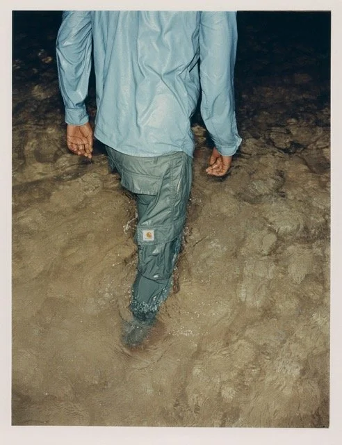 Person walking through shallow water at night, wearing a gray jacket and pants.