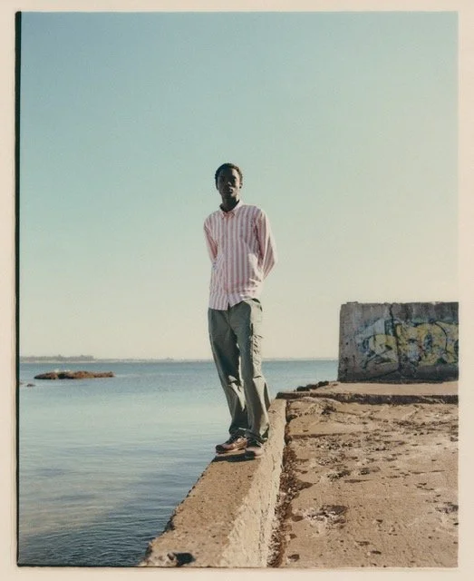 A person standing on the edge of a concrete pier by the water under a clear sky, with graffiti on a nearby concrete block.