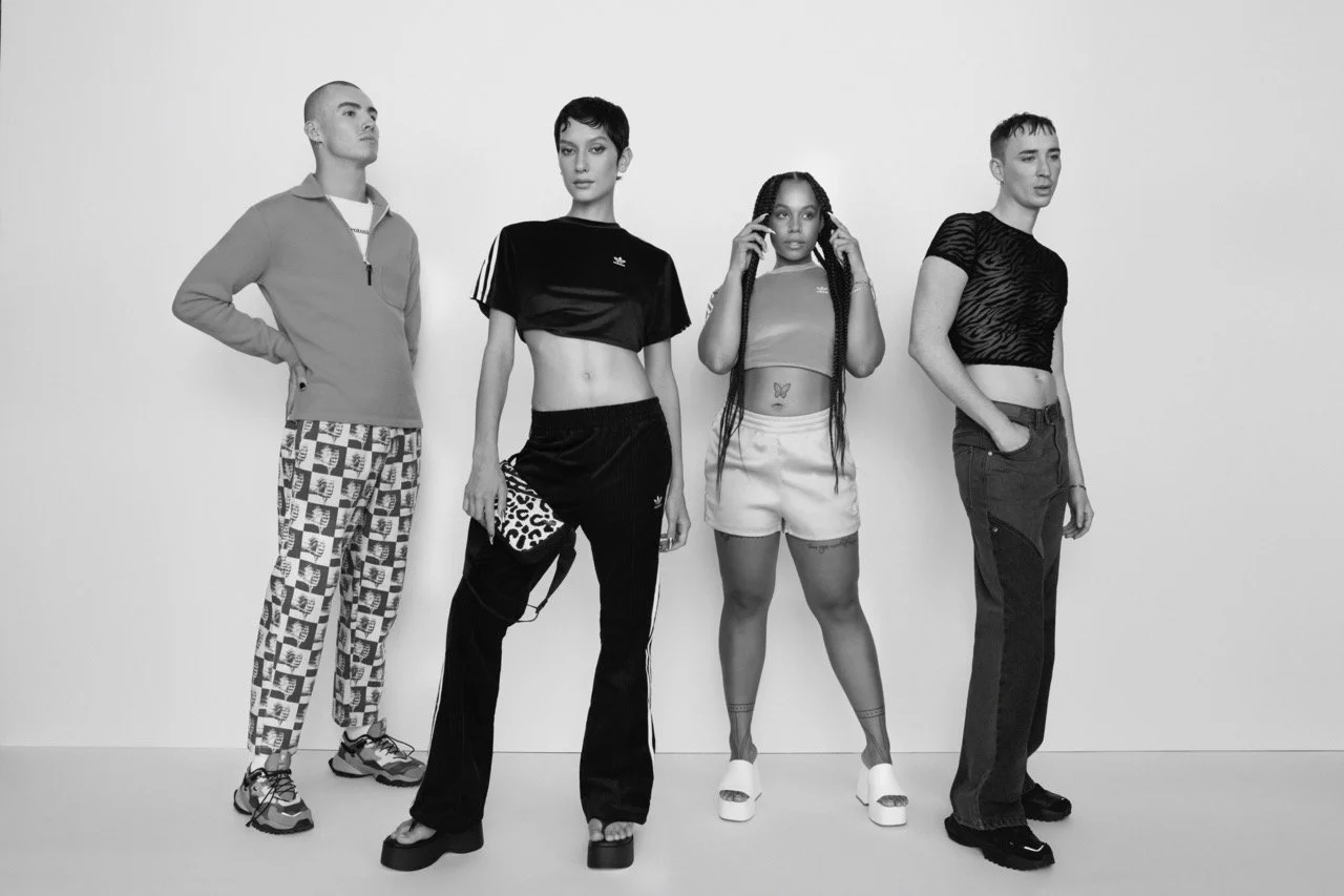 Four individuals standing in a row against a plain background, dressed in casual, trendy clothing in a black-and-white photo.