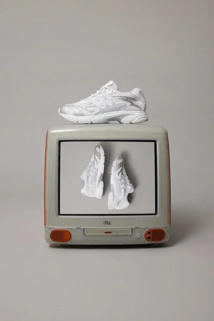 White athletic sneakers placed on top of a vintage beige and orange store monitor displaying an image of the same sneakers.