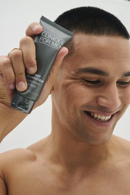 A smiling man holding a tube of Clinique for Men moisturizer next to his face.