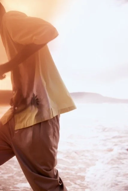 Person standing on a beach during sunset, wearing tan pants and a tan jacket.