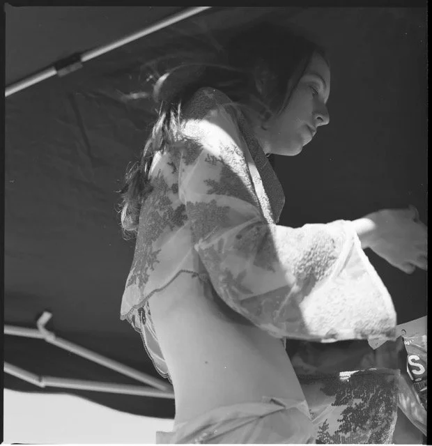 A woman in a coat with a hood, looking down at something, under an umbrella or canopy.