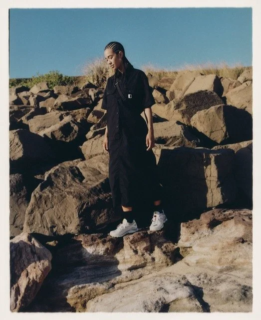 A woman standing on large rocks outdoors with a clear blue sky in the background.