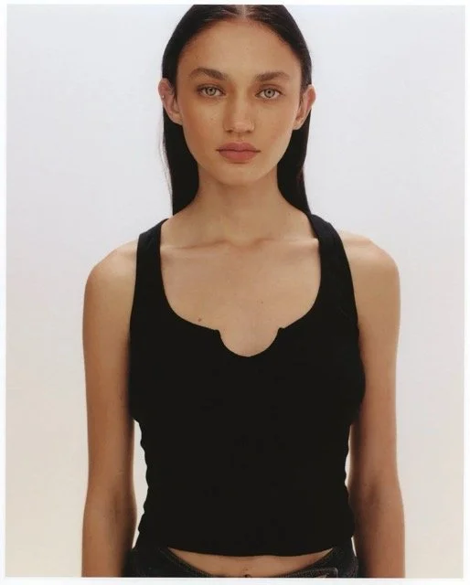 Young woman with dark hair in a black tank top against a plain white background.