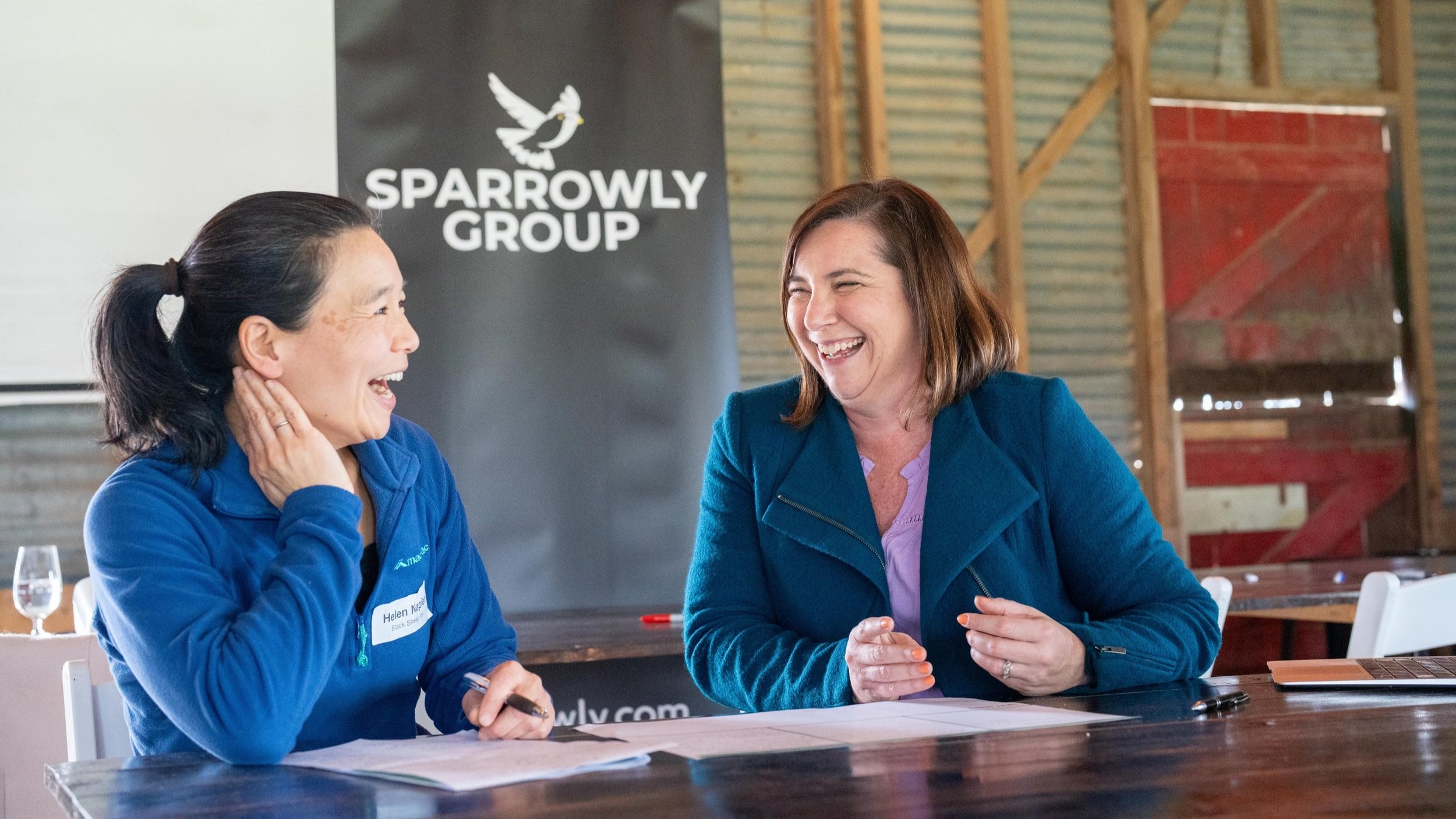 Naomi Farrelly laughing with a women sitting infront of the Sparrowly Group logo.