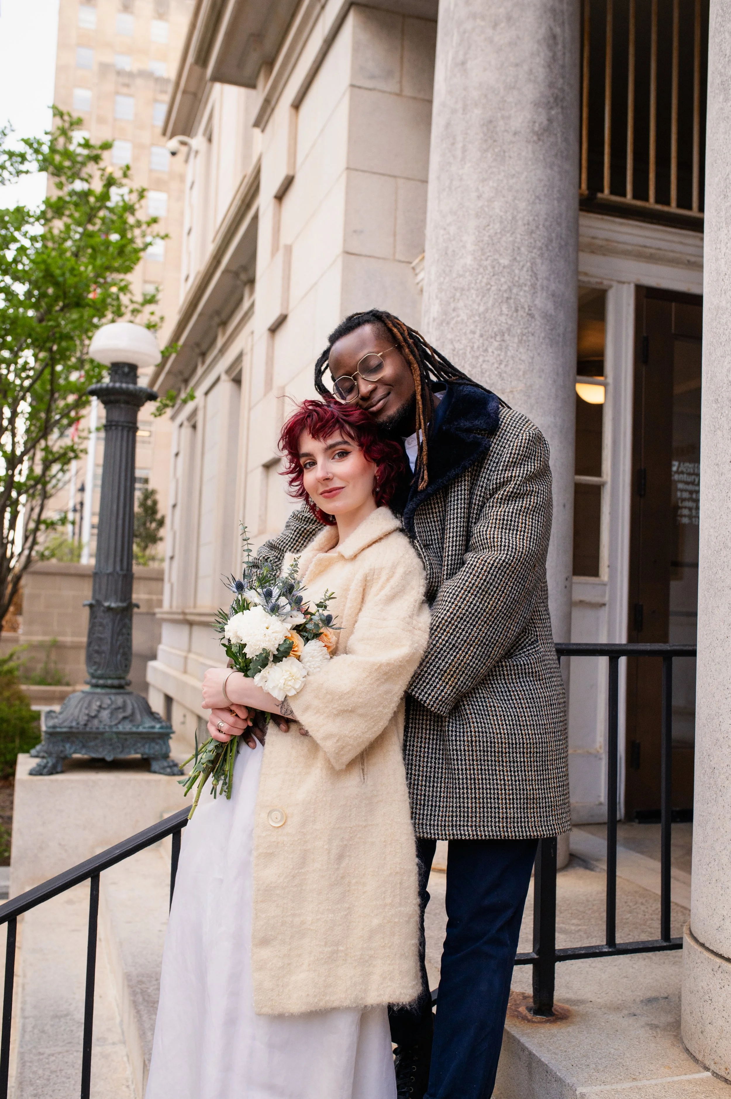 A newly married couple snuggle in front of a Second Empire building in downtown Raleigh.