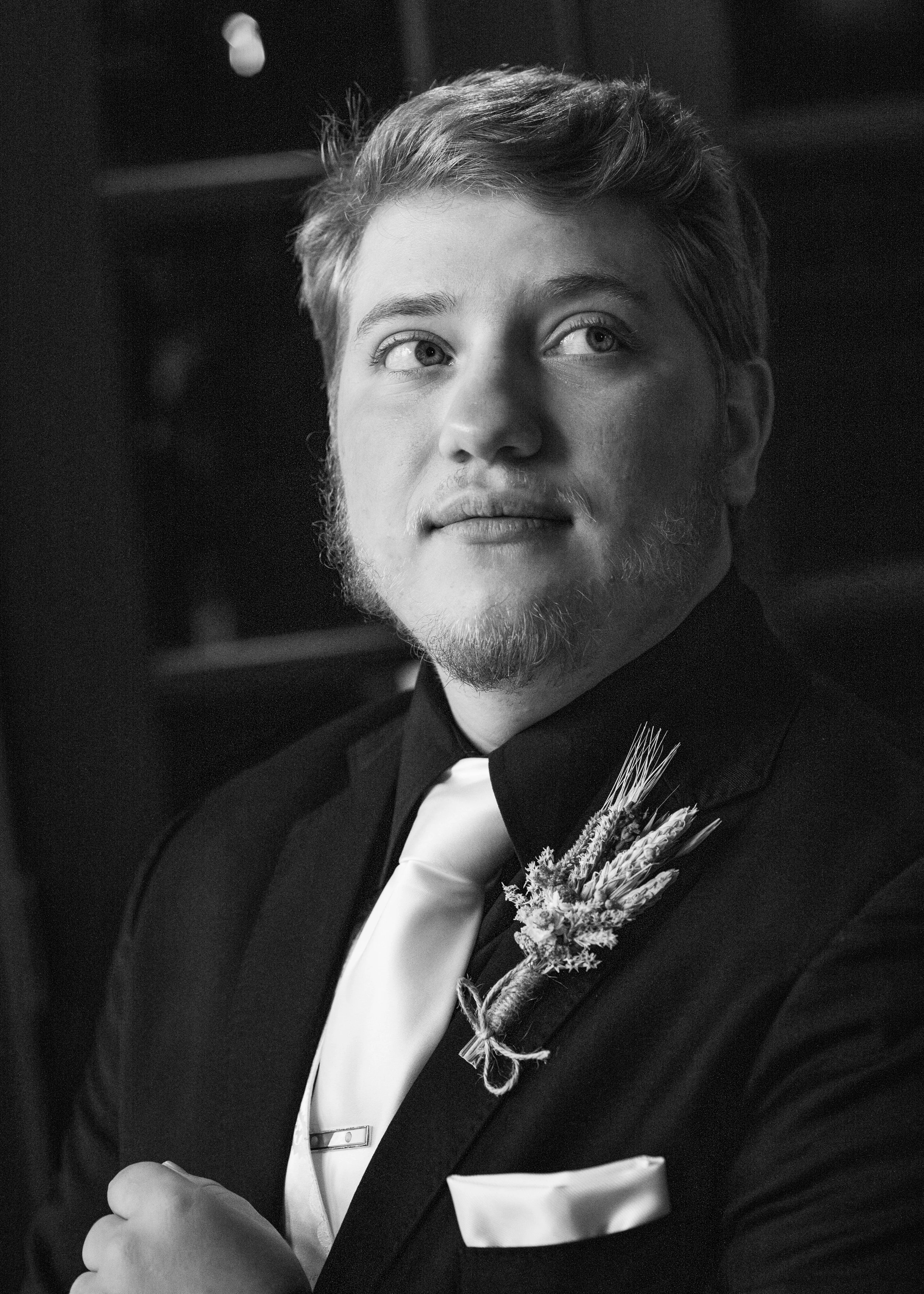 The groom is dressed for the wedding ceremony, adjusting his suit, and looking to the right.
