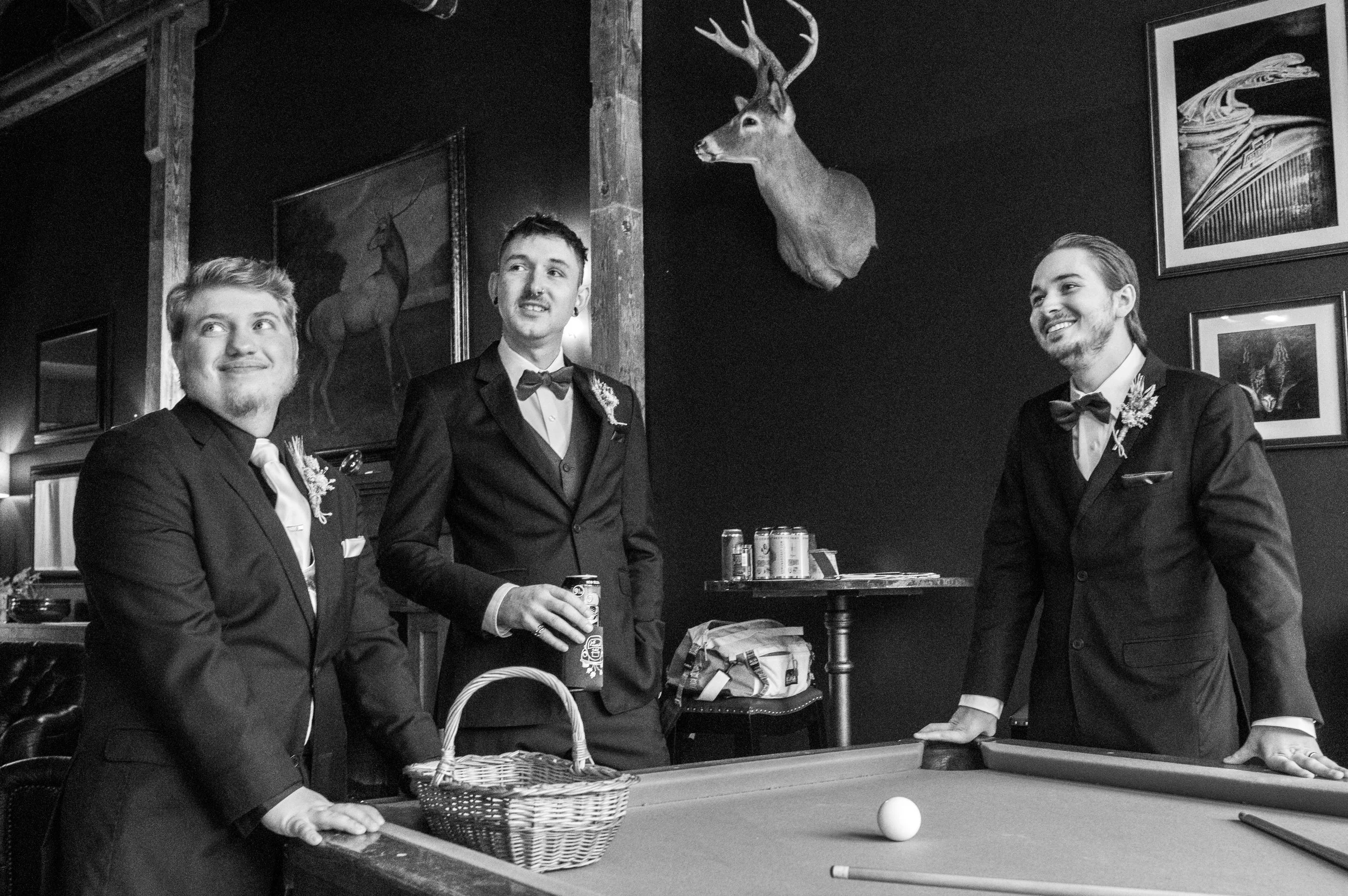 The groom and his groomsmen, dressed and ready for the wedding ceremony, gather around a pool table.