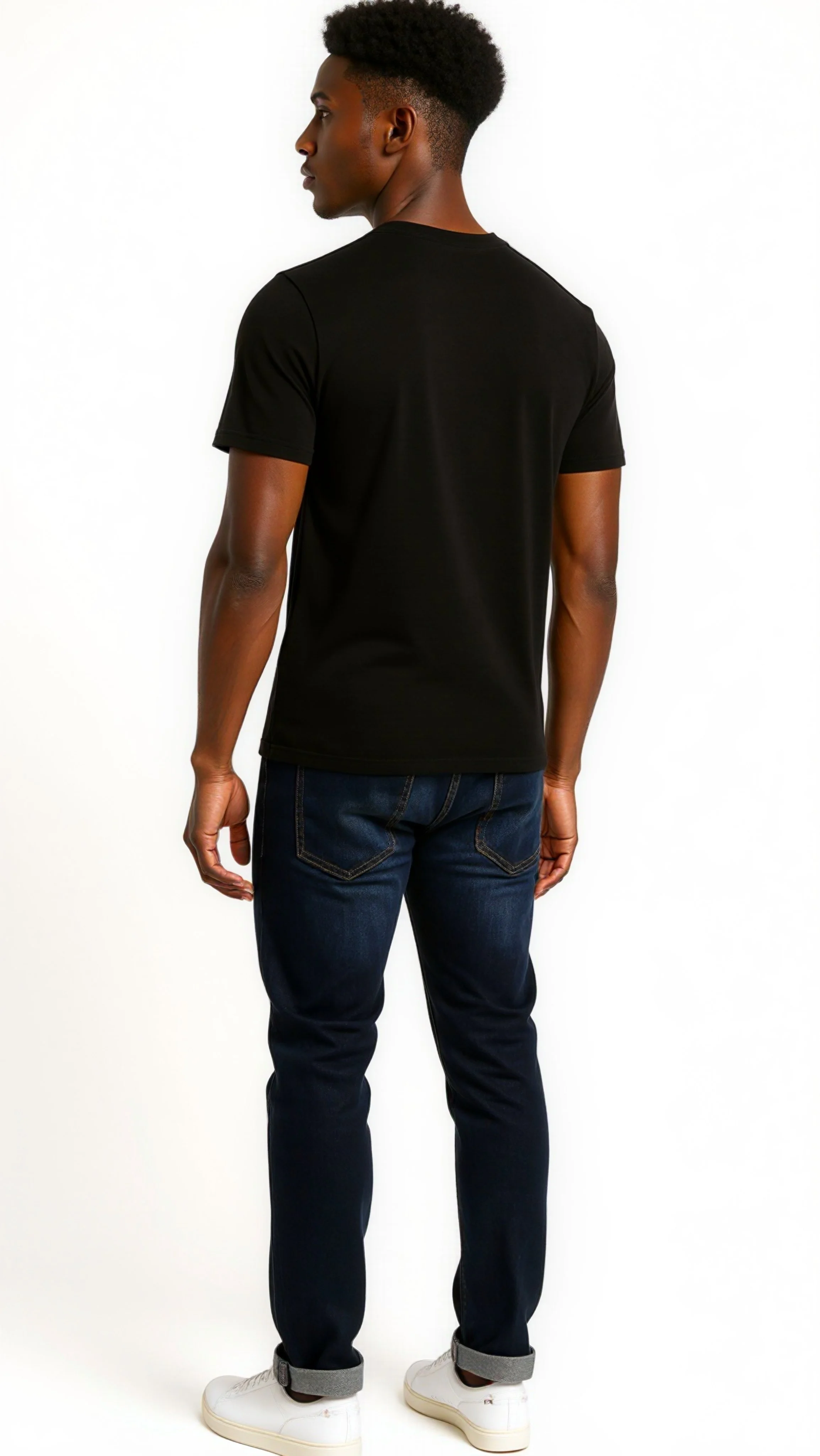 A young man with short black hair, wearing a black t-shirt, dark jeans, and white sneakers, standing against a plain white background, facing away from the camera.