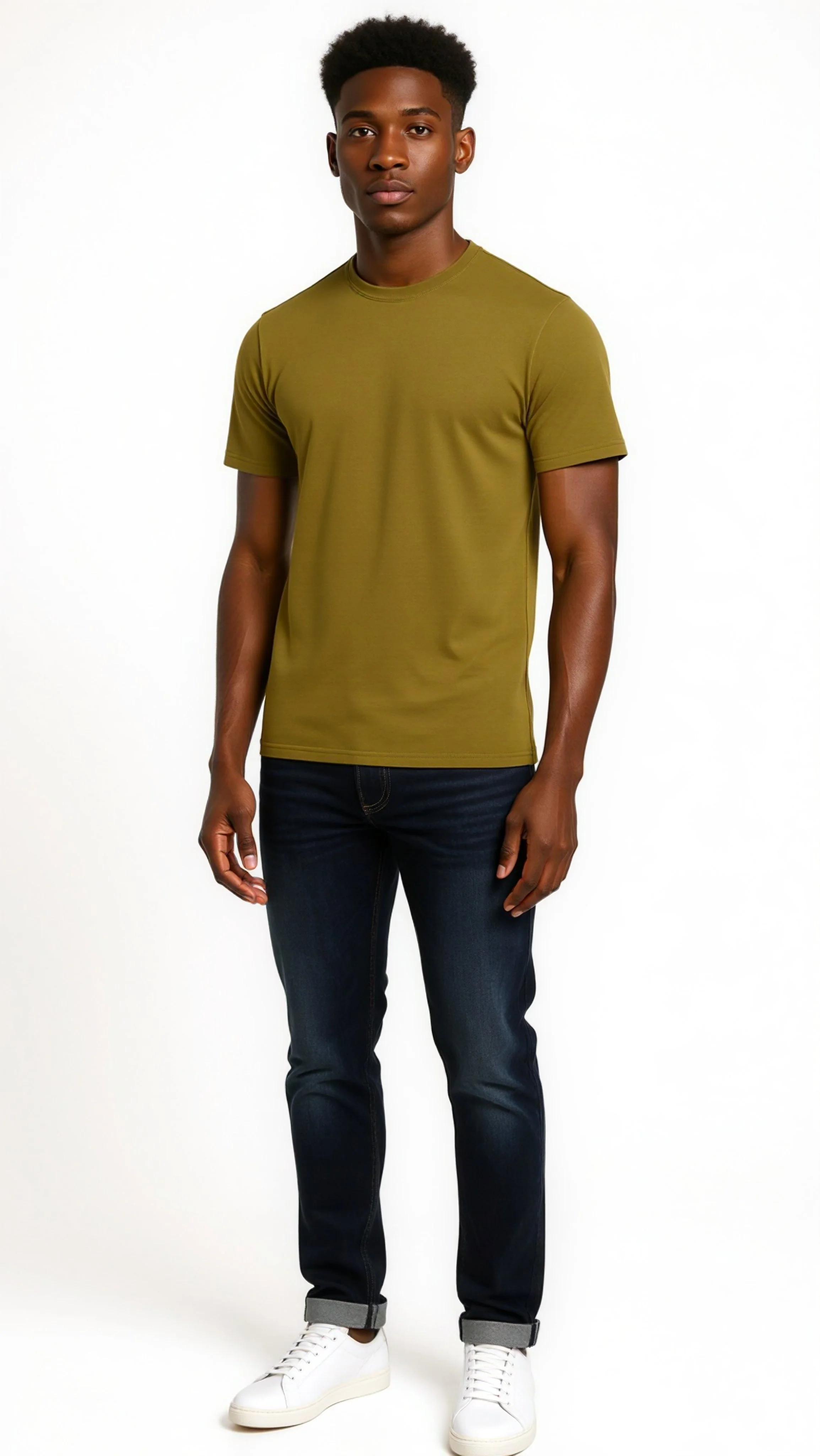 A young man with dark skin, short curly hair, wearing a plain olive green T-shirt, dark blue jeans, and white sneakers standing against a plain white background.