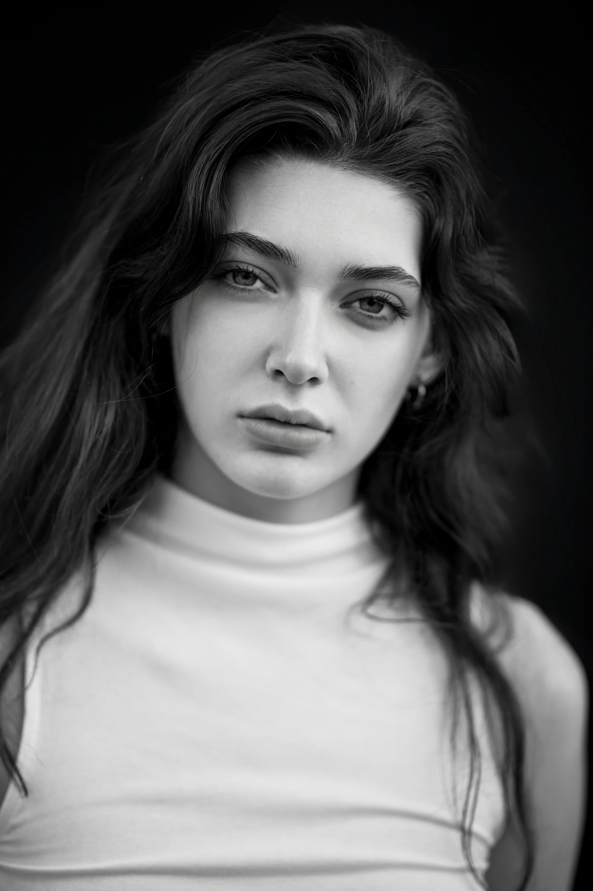 Black and white portrait of a young woman with long wavy hair, wearing a high-neck sleeveless top, with a neutral expression.